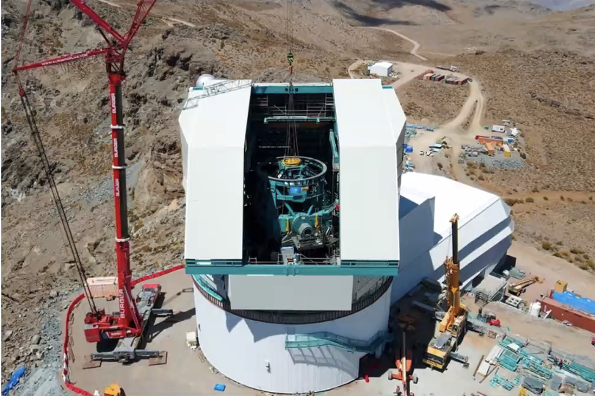 Ongoing construction of the Vera C Rubin Telescope. A crane is lifting large machinery into the dome.