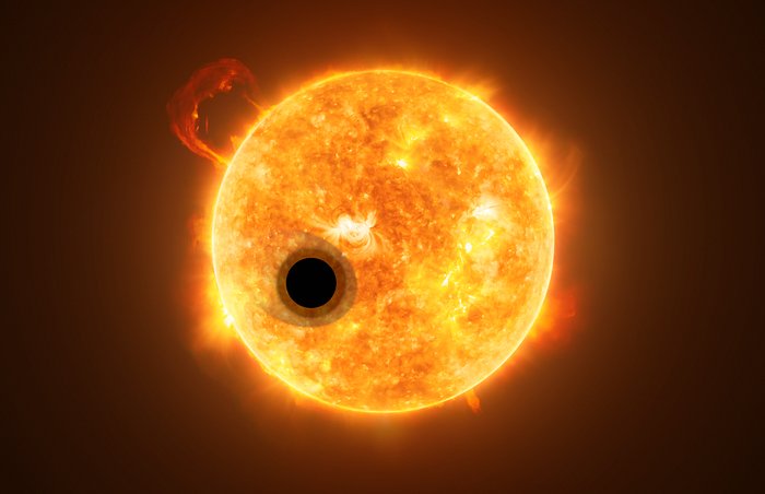 Illustration of a giant planet with a fuzzy surrounding layer passing in front of the face of an active yellow star.