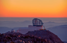 Photo of a telescope dome and associated building on a tall mountaintop at sunset.