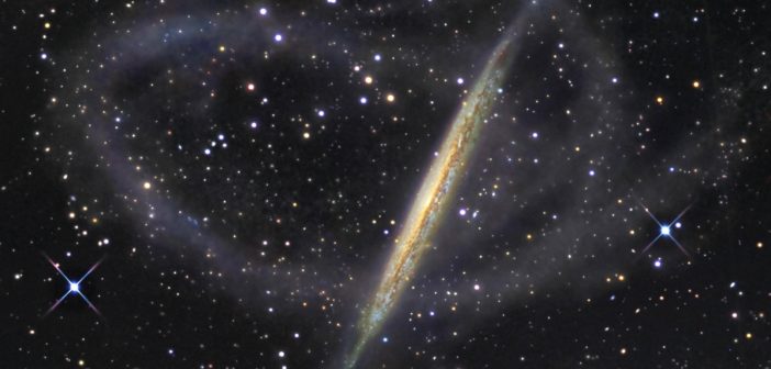 Photo of an edge-on galaxy encircled by a faint stream of stars.