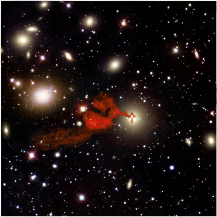 Photograph of radio emission from a jet composited with a cluster of bright galaxies.