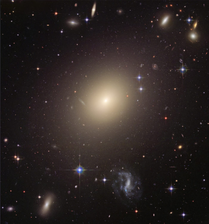 Photograph of a large, bright, elliptical galaxy in the midst of a broader galaxy field.