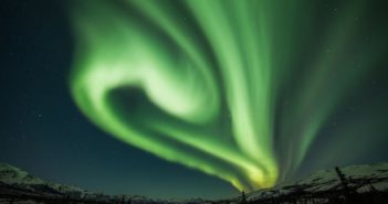 Curtains of green light hang in the sky above a snowy Alaskan landscape