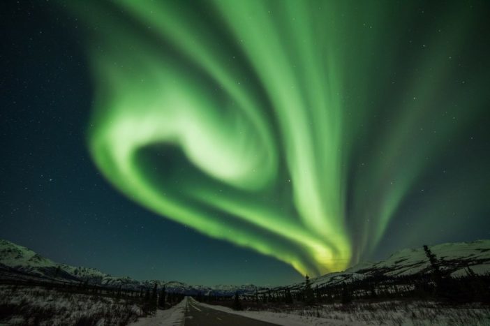 Curtains of green light hang in the sky above a snowy Alaskan landscape