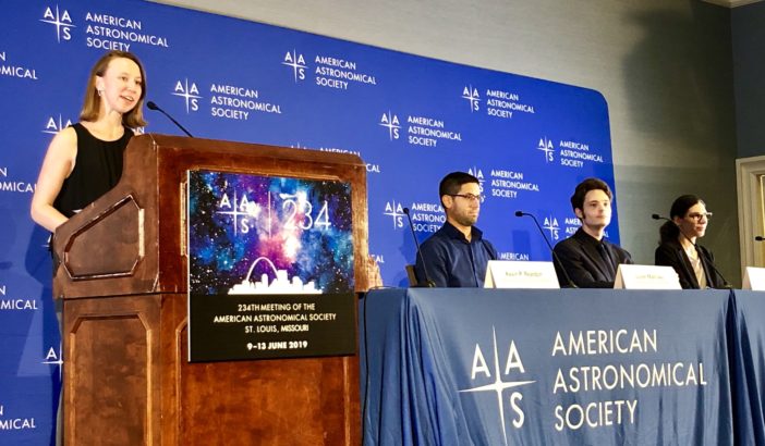 Photograph of a female speaker at a podium next to a row of seated panelists behind a banner that reads "American Astronomical Society"