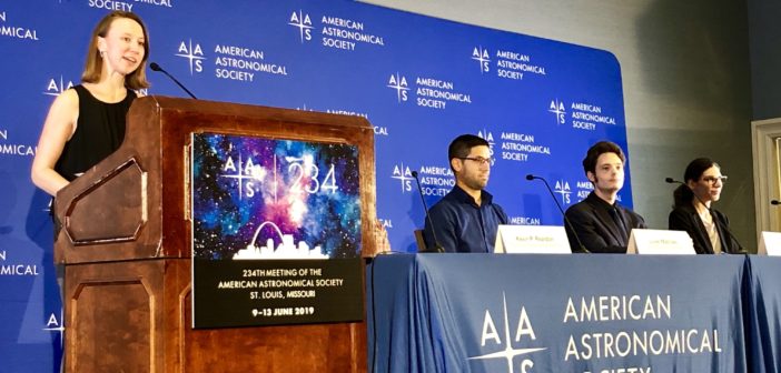 Photograph of a female speaker at a podium next to a row of seated panelists behind a banner that reads "American Astronomical Society"