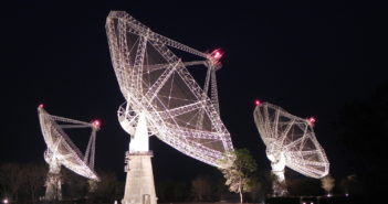 Photograph taken at night showing three radio dishes in part of an array.