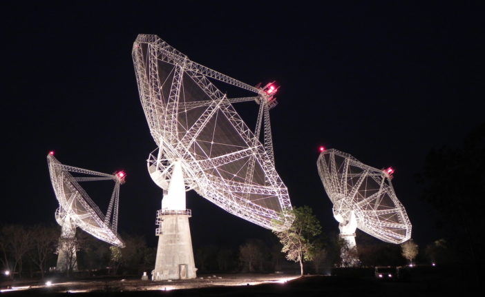 Photograph taken at night showing three radio dishes in part of an array.