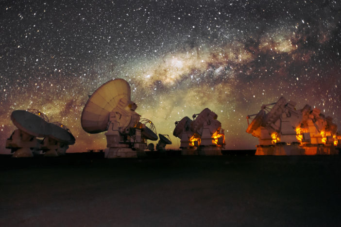 More than 10 radio telescopes point toward the sky in front of the Milky Way