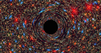 Simulated image showing a foreground black hole warping spacetime around it, with a background of red and blue stars in the center of a galaxy.