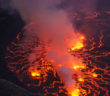 cooled black lava is crossed by bright cracks showing hotter lava below. gas billows from multiple bright areas.