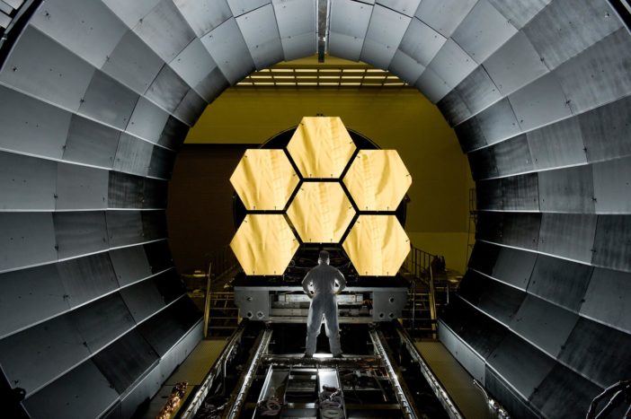 photograph of an engineer standing in front of JWST mirror segments