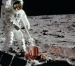 A photograph of an astronaut on the lunar surface standing over an instrument with large solar panels