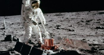 A photograph of an astronaut on the lunar surface standing over an instrument with large solar panels