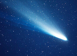 A photograph of a comet against a background of many stars. The bright core is near the bottom-right, and the tail extends towards the upper-left, growing increasingly wispy and wide with distance to the core.