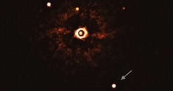 A photograph of a masked-out star surrounded by a halo of light leaking around the edge of the mask. Surrounding the halo are smaller star-like dots, one of which is annotated with an arrow. This is the directly imaged planet, and the other dots are faint background stars.