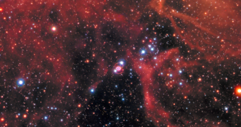 An image of the night sky featuring a wispy gas cloud and many stars. Tiny and at the center, the supernova remnant is flanked by a pair of rings of debris.