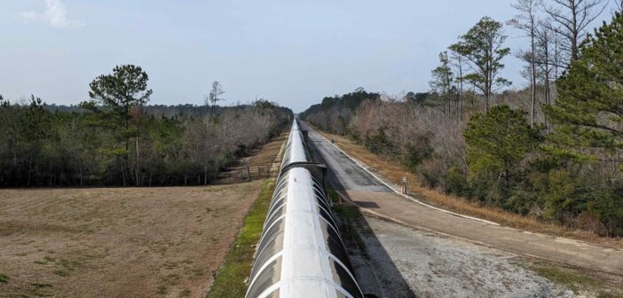 A photograph of a concrete tube extending to the horizon into low shrubs and swamp.