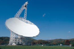 A photograph of a 100m radio dish in an otherwise empty field.