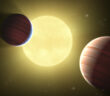 A rendering of two dark planets in front of a bright yellow star.