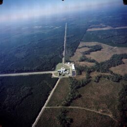 A photograph of two perpendicular straight lines that cut through a forest and meet at a complex of buildings in a clearing.