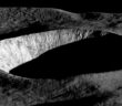 An oblique-angle photograph of a deep crater half in shadow.